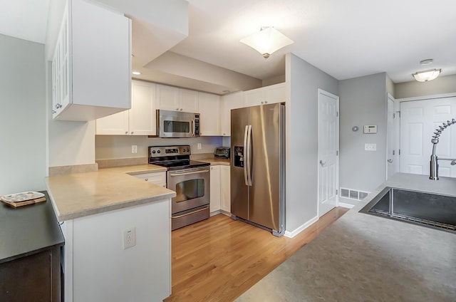 kitchen with kitchen peninsula, appliances with stainless steel finishes, light wood-type flooring, sink, and white cabinetry