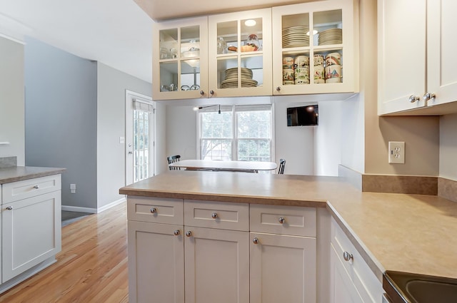 kitchen featuring kitchen peninsula, white cabinets, light hardwood / wood-style floors, and stainless steel range oven