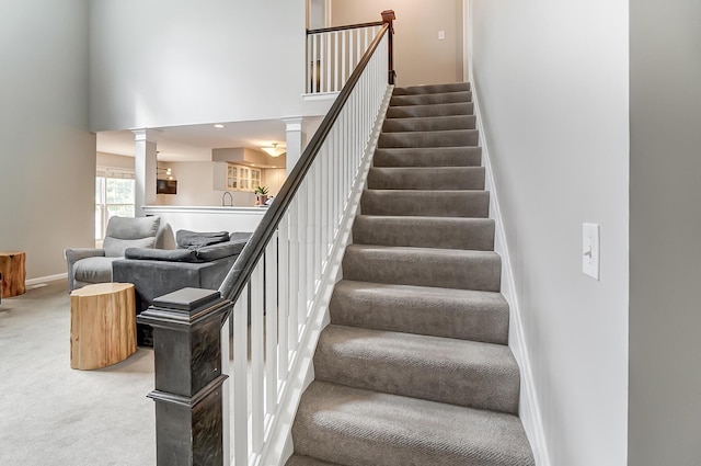 stairs featuring a towering ceiling, carpet floors, and decorative columns