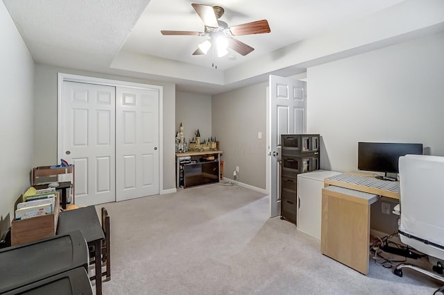 carpeted office with a raised ceiling and ceiling fan