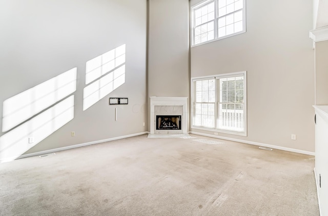 unfurnished living room featuring light carpet, a towering ceiling, and a high end fireplace