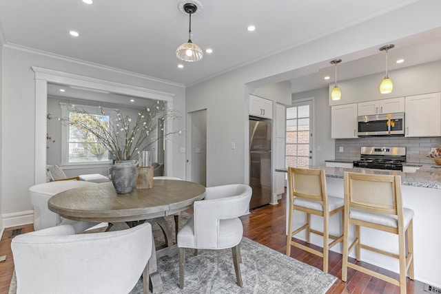 dining space with dark wood-type flooring, ornamental molding, and a wealth of natural light