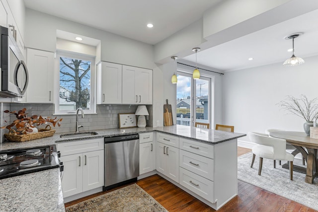 kitchen with appliances with stainless steel finishes, white cabinetry, hanging light fixtures, kitchen peninsula, and light stone countertops