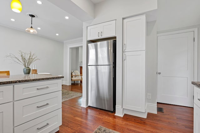 kitchen featuring stainless steel fridge, white cabinetry, dark hardwood / wood-style floors, decorative light fixtures, and dark stone counters