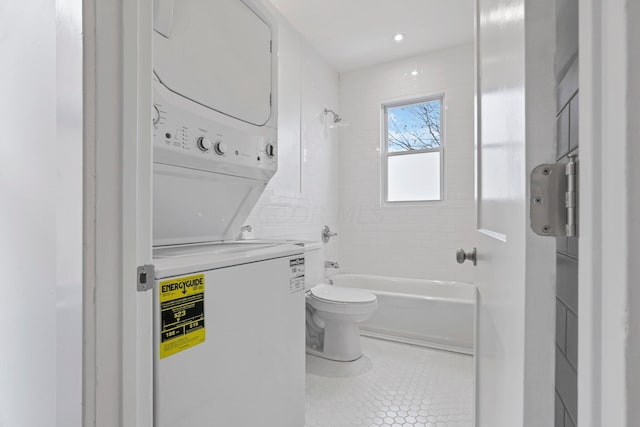 bathroom with tiled shower / bath combo, stacked washer / drying machine, tile patterned floors, and toilet