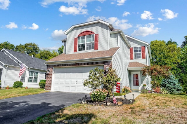 traditional home featuring a shingled roof, aphalt driveway, an attached garage, a front lawn, and brick siding