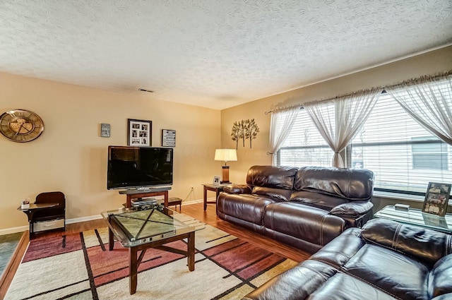 living area featuring a textured ceiling, wood finished floors, visible vents, and baseboards