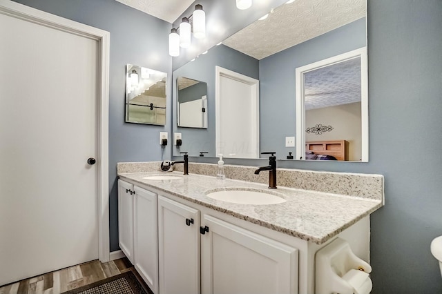 bathroom featuring double vanity, a sink, a textured ceiling, and wood finished floors