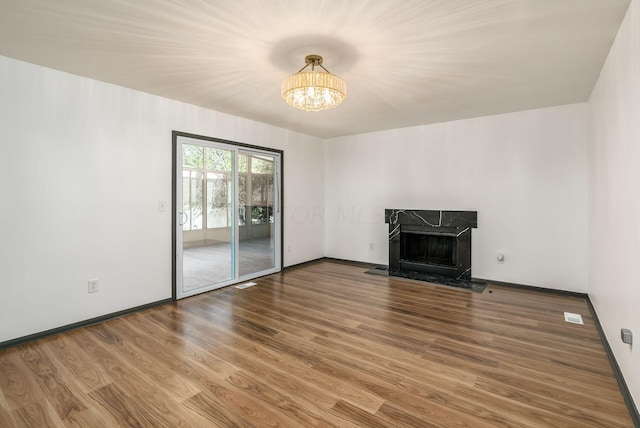 unfurnished living room with wood-type flooring, a notable chandelier, and a premium fireplace