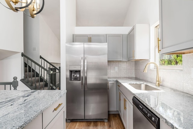 kitchen featuring light stone countertops, appliances with stainless steel finishes, light wood-type flooring, sink, and a notable chandelier