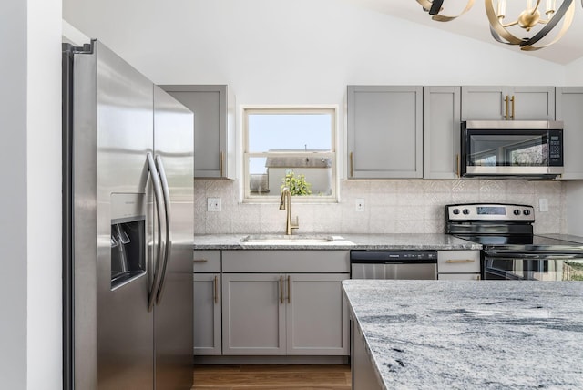 kitchen featuring lofted ceiling, backsplash, sink, light stone countertops, and stainless steel appliances