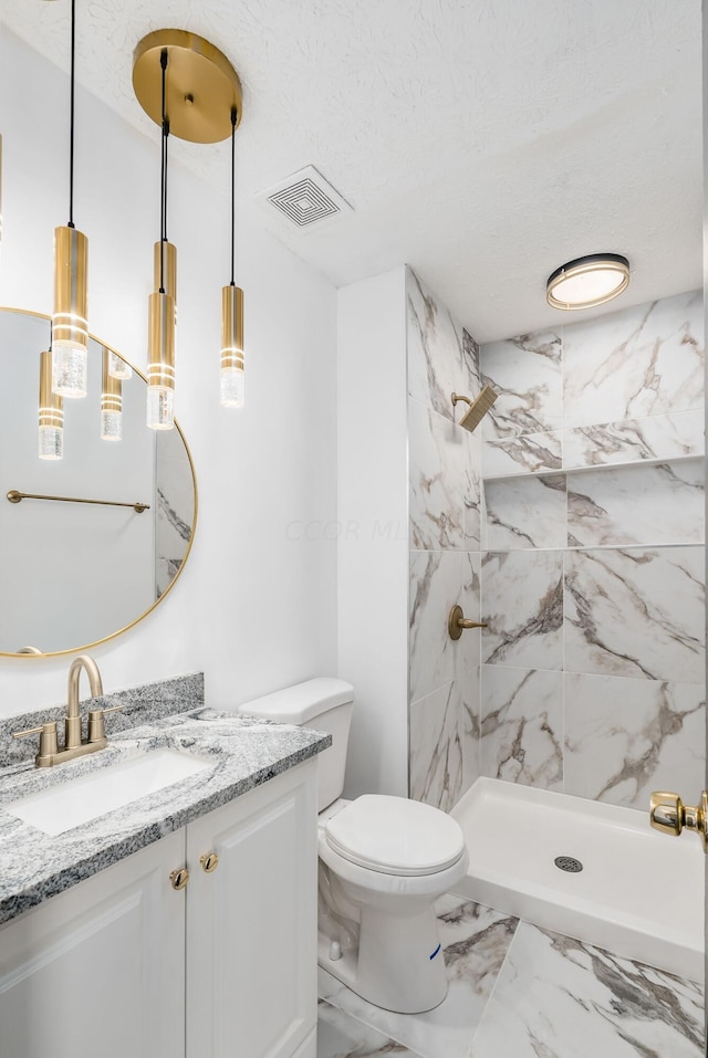 bathroom with vanity, toilet, a tile shower, and a textured ceiling