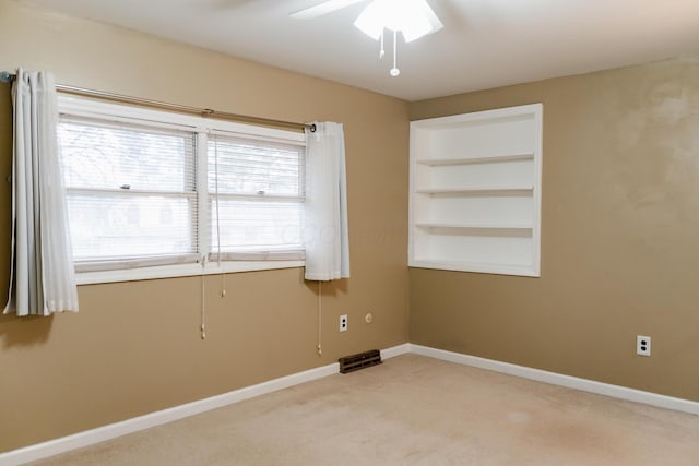 carpeted empty room featuring ceiling fan and built in shelves