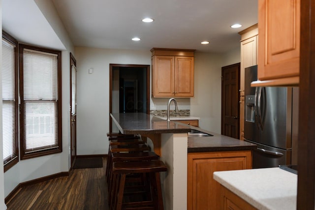 kitchen featuring sink, dark wood-type flooring, stainless steel fridge, and a kitchen bar