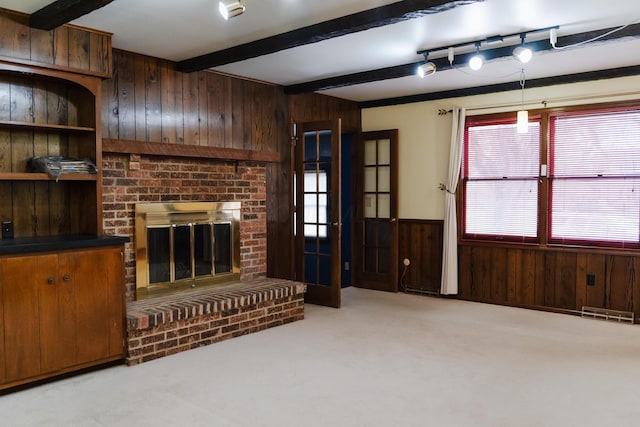 living room with wood walls, track lighting, a brick fireplace, light carpet, and beam ceiling