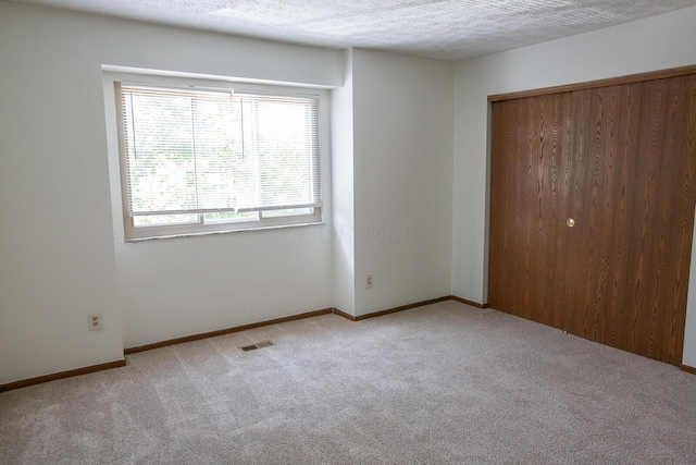 unfurnished bedroom featuring light carpet, a closet, and a textured ceiling