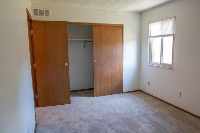 unfurnished bedroom with light carpet, a closet, and a textured ceiling