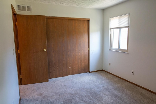 unfurnished bedroom with a closet, light colored carpet, and a textured ceiling