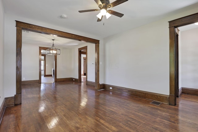 spare room featuring ceiling fan with notable chandelier and dark wood-type flooring