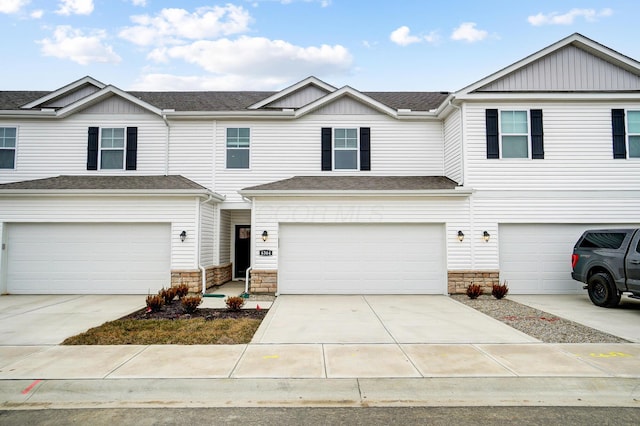 townhome / multi-family property featuring a garage, stone siding, driveway, and roof with shingles