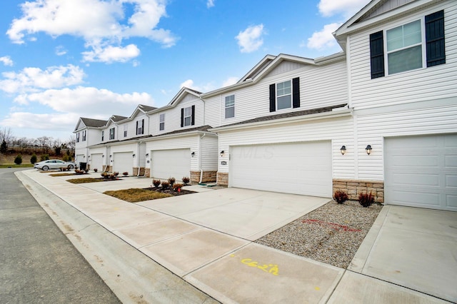 view of front of house featuring stone siding, driveway, an attached garage, and a residential view