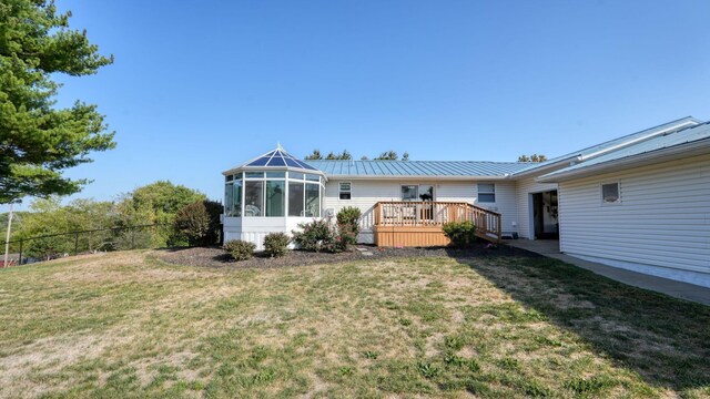 back of property featuring a sunroom, a deck, and a lawn