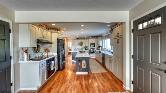 kitchen with a kitchen bar, appliances with stainless steel finishes, a textured ceiling, light hardwood / wood-style flooring, and a center island