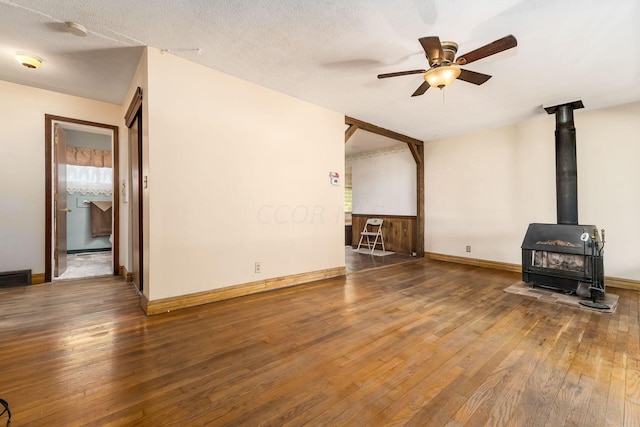 unfurnished living room with a wood stove, ceiling fan, dark wood-type flooring, and a textured ceiling