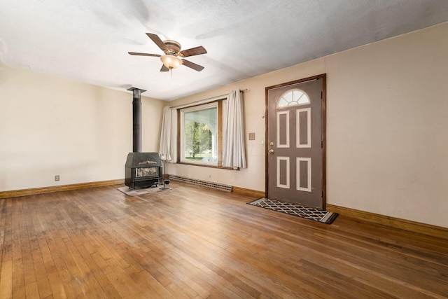 foyer with a wood stove, ceiling fan, a baseboard heating unit, hardwood / wood-style floors, and a textured ceiling