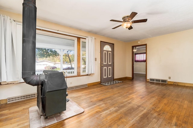 interior space featuring a wood stove, ceiling fan, a baseboard radiator, and hardwood / wood-style flooring