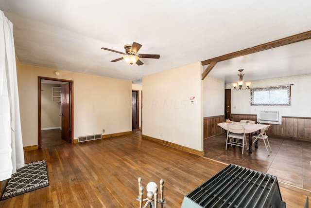 living room featuring ceiling fan with notable chandelier, wooden walls, a wall unit AC, and dark wood-type flooring