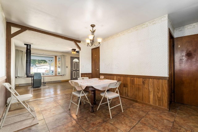 tiled dining area featuring ceiling fan with notable chandelier, a wood stove, and wooden walls