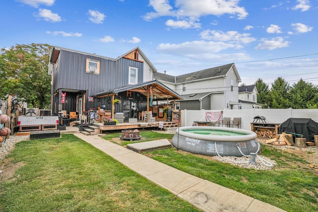 rear view of house featuring a lawn, a swimming pool side deck, and a fire pit