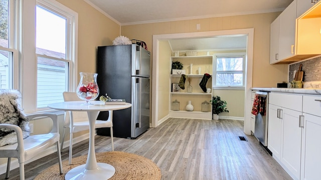 kitchen with tasteful backsplash, crown molding, light hardwood / wood-style floors, white cabinets, and appliances with stainless steel finishes