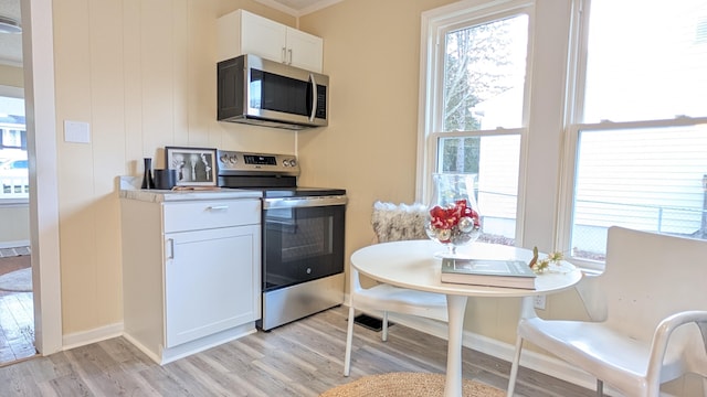 kitchen featuring ornamental molding, white cabinets, light wood-type flooring, and appliances with stainless steel finishes