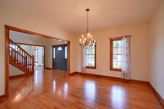 empty room with light hardwood / wood-style floors and an inviting chandelier