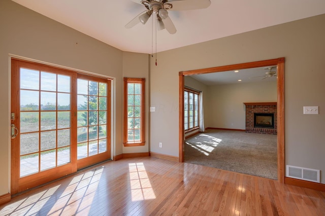 doorway with a fireplace, light wood-type flooring, and ceiling fan