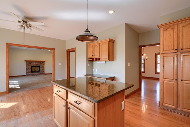 kitchen with dark stone counters, a fireplace, light hardwood / wood-style floors, a kitchen island, and hanging light fixtures