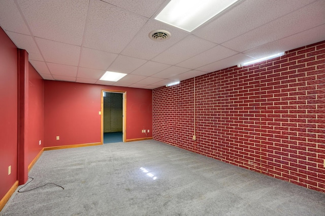 basement with carpet flooring, a drop ceiling, and brick wall