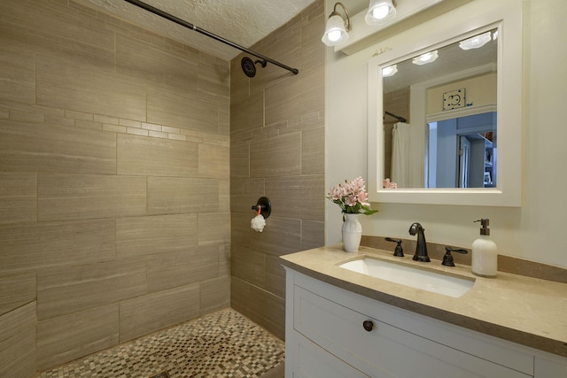 bathroom featuring a textured ceiling, vanity, and a tile shower