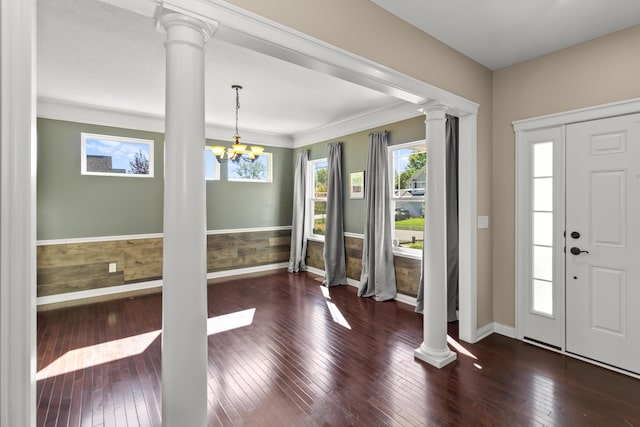 entrance foyer with a chandelier, decorative columns, crown molding, and dark wood-type flooring