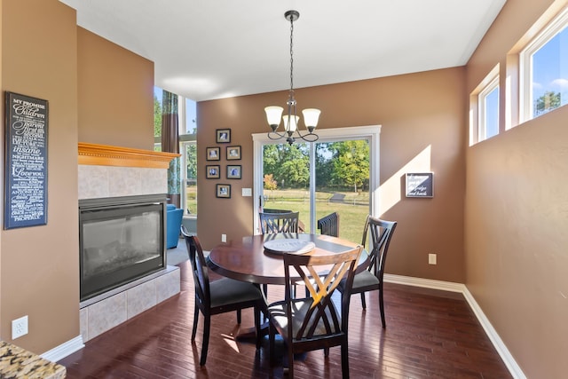 dining space featuring dark wood-type flooring, a tile fireplace, and an inviting chandelier