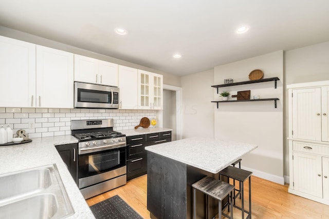 kitchen with a kitchen breakfast bar, white cabinetry, light hardwood / wood-style flooring, and appliances with stainless steel finishes