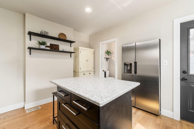 kitchen with stainless steel refrigerator with ice dispenser, light hardwood / wood-style floors, a kitchen island, a kitchen bar, and dark brown cabinetry