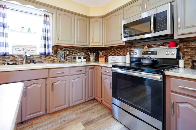 kitchen with tasteful backsplash, sink, light hardwood / wood-style floors, and appliances with stainless steel finishes