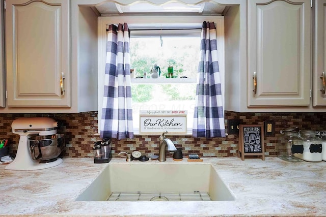 kitchen featuring tasteful backsplash, light stone counters, and sink