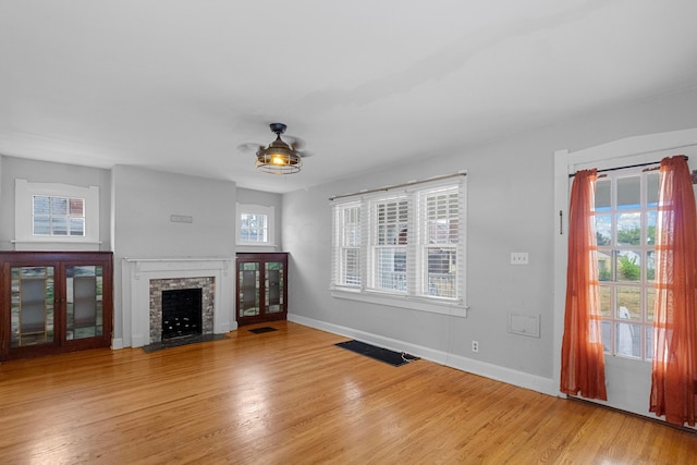 unfurnished living room featuring hardwood / wood-style flooring, a stone fireplace, and a healthy amount of sunlight