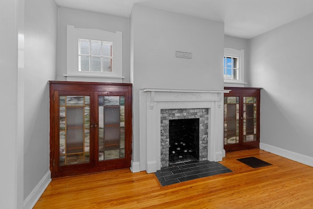 unfurnished living room with a brick fireplace, french doors, and hardwood / wood-style flooring