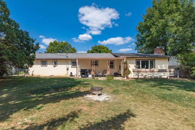 rear view of property featuring a yard, a patio, and a fire pit