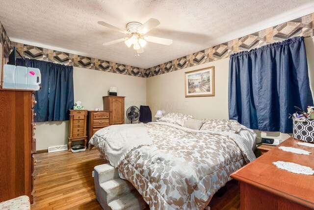 bedroom with ceiling fan, wood-type flooring, and a textured ceiling